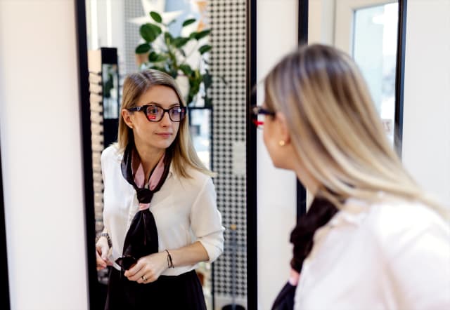Kobieta przymierza okulary przed lustrem